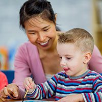 Teacher helping a toddler with a craft.