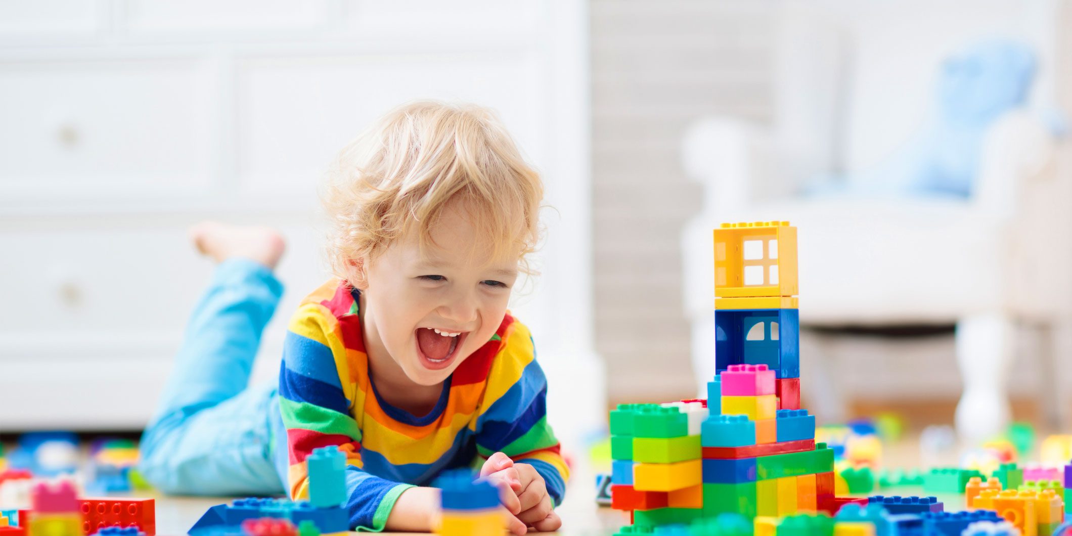 Young child smiling and laughing on the floor with colorful building blocks.